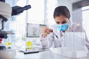 Cant afford to make mistakes. a focused young female scientist wearing a surgical mask and doing an experiment while being seated inside a laboratory.