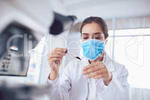 I have to be super careful right now. a focused young female scientist wearing a surgical mask and doing an experiment while being seated inside a laboratory.