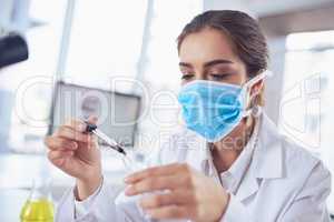This is where the concentration comes in. a focused young female scientist wearing a surgical mask and doing an experiment while being seated inside a laboratory.