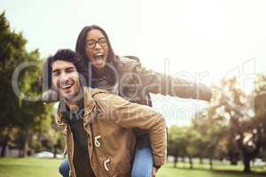 We are wild and free. Portrait of a cheerful young couple having a piggyback ride while looking at the camera outside in a park.