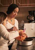 Gently pour mixture into pan. two determined young women baking together in a kitchen at home.