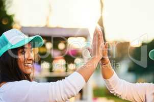 Thats another sale made. a cheerful young woman giving another person a high five outside during the day.