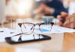 We see everything in a different way as creatives. Closeup of a pair of reading glasses on a wooden table outside in a coffeeshop.