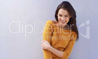 Her laugh is infectious. Portrait of a beautiful young woman laughing while standing against a gray wall.