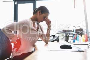 Feeling the aches and pains hit her body all over. a young businesswoman suffering from a headache and back pain while working in an office.