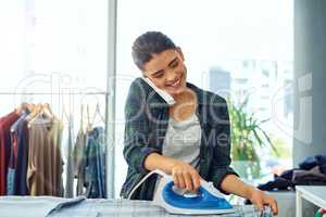 Ill be free after the ironing. an attractive young woman using her cellphone while doing the ironing at home.