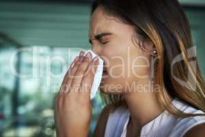 Trying to beat the flu. a young businesswoman blowing her nose in an office.
