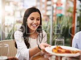 Why thank you kind sir. a cheerful young woman receiving a slice of pizza while being seated next to a table at a restaurant outside.