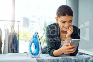 Making plans now that the cleanings done. an attractive young woman using her cellphone while doing the ironing at home.