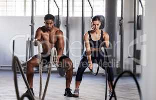 Active, fitness partners training together, exercising with battle ropes in gym. Athletic sports couple in motion doing arms and cardio workout in wellness center for strength and healthy lifestyle.