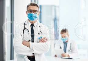 Doctor, physician or healthcare professional with covid face mask in a hospital for medical health insurance background. Innovation, leadership and excellence male gp portrait with his arms crossed