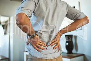 Theres a bit of pain at my lower back. Rearview shot of an unrecognizable man holding his back in discomfort due to pain inside at home.