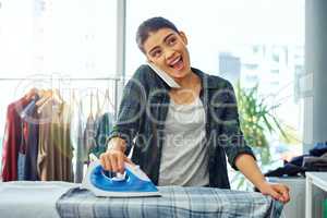 Im just finishing up the ironing. an attractive young woman using her cellphone while doing the ironing at home.