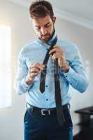 The way to make the perfect tie. a handsome young man putting on a tie in his bedroom at home.