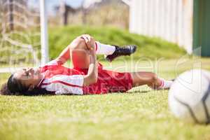 Injured, pain or injury of a female soccer player lying on a field holding her knee during a match. Hurt woman footballer with a painful leg on the ground in agony having a bad day on the pitch