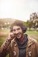 We can talk for hours. a cheerful young man talking on his phone while standing outside in a park.