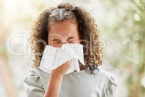 Sick little girl with a flu, blowing her nose and looking uncomfortable. Child suffering with sinus, allergies or covid symptoms and feeling unwell. Kid with a cold sneezing and holding a tissue