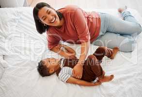 Mother playing, bonding and laughing with her son playful, fun and funny moments together on the bed at home. Parenting and enjoying quality, happy single mom and her child in kids bedroom.