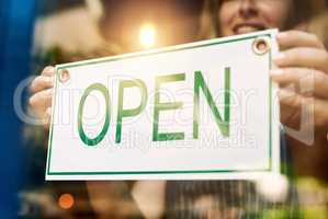 Open for business and ready for customers. an unrecognizable woman holding up a open sign at a bar.