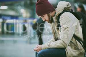 Passing the time with some of his favourite tunes. a handsome young man listening to music on his cellphone while sitting in a bus station.