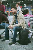 Public transport is his preferred method of travel. Full length shot of a handsome young man listening to music on his cellphone while sitting in a bus station.
