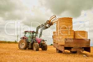 Keeping his farm neat and tidy. a farmer stacking hale bales with a tractor on his farm.