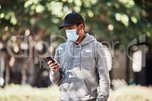 Man looking at phone in nature park, wearing face mask to prevent risk of covid and reading a text message online. Guy standing in garden outside, typing on social media and looking for gps location
