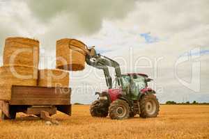 Stack em up. a farmer stacking hale bales with a tractor on his farm.