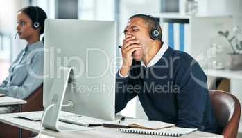 Tired call center agent yawning while sitting at his desk working on a computer in the office. Exhausted, bored and rude man in financial customer service feeling fatigue after a long day at work.