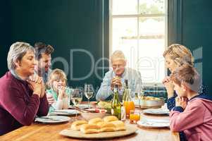 We are thankful to have each other. a peaceful family seated around the dinner table and saying grace with eyes closed at home.