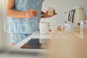 Casual woman adding sugar while preparing a cup of coffee, tea or hot chocolate in the kitchen during the morning. Female hands holding teaspoon for a fresh beverage in a mug for breakfast at home