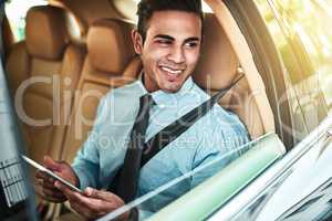 Staying productive during his daily commute. a young businessman using a digital tablet while sitting in the back seat of a car.