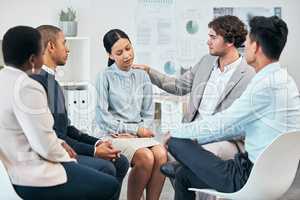 Diverse colleagues support and comfort unhappy, sad coworker at team meeting or gathering. Compassionate, caring employees showing empathy to distressed woman in work group therapy session.