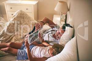 Exploring the online world in comfort together. a father and his little son using a digital tablet while lying in bed at home.