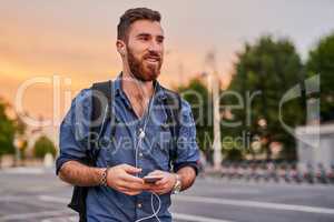 Hes on the move with technology. a handsome young man listening to music on his cellphone while walking through the city.