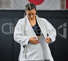 . Female professional karate student dressing, wearing and preparing for practice, fight or training match in dojo. Woman mix martial art athlete tying uniform before competition or exercise workout.