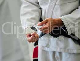 . Karate master tying a belt on a student in a dojo before practice. Closeup of a sensei help, prepare and assisting a beginner before exercise, workout and training in a sport club.