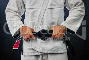 . Professional karate master holding a black belt against a dark background in a dojo. Trainer, coach or leader prepared and motivated for training, fitness exercise and fight practice in a dojo.