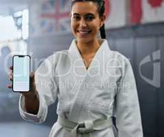 Portrait of a female karate student holding tech with social media, looking active and fit at class. Blank screen on phone, showing a fitness app and training website while standing at a sports gym.