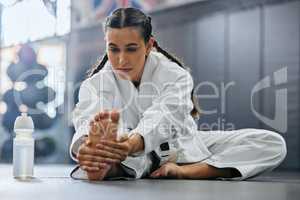 . Female karate school student doing a warmup, stretch or exercise with serious, determine and focus before workout. Sports woman or coach leg stretching at a dojo studio, gym or martial arts club.