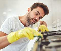 Really getting in there. a handsome young man carefully cleaning the stove in his kitchen.