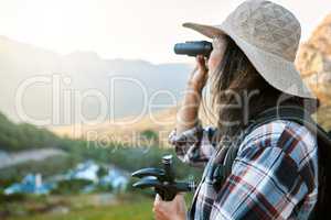 Hiking, exploration and mountain adventure with binoculars, trekking pole and walking aid in a remote landscape with view. Mature woman, hiker and tourist watching birdlife or wildlife in eco nature