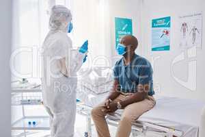 Doctor consulting a patient with covid, sickness or disease in a healthcare facility or clinic. Medical professional in a hazmat suit writing a patients symptoms on a chart in a hospital check up