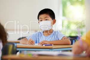. Face mask to protect from covid during pandemic, creative school student learning in class and writing in notebook in classroom. Boy sitting at a desk, doing education task and studying with books.