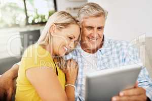 Happy, relaxed and in love mature couple watching a movie together on a tablet online while relaxing on a couch indoors at home. Smiling senior man and woman streaming their entertainment tv series