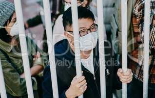 Sick, trapped young covid patient stuck in the city feeling like a prisoner, wearing a medical face mask. Foreign asian man in a crowd during a pandemic. Male following city healthcare safety rules.