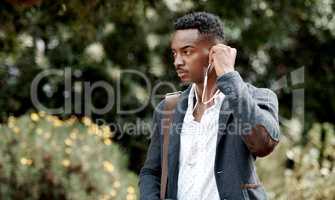 A stylish, trendy and serious young man going to work while listening to music using earphones. A young African American male entrepreneur walking outdoors with nice style or fashion