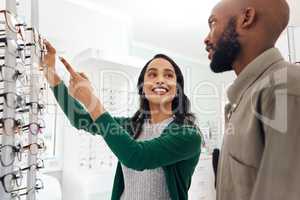 Smiling optometrist assisting man with glasses in a modern sale optometry store. Attractive lady in customer service helping young, African and healthy male choose and buy eyewear in a shop.