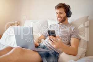 5g internet, video and online streaming of a man on a computer and phone in bed. Happy guy with a smile relax and multitask listening to a digital radio podcast or web music with modern technology