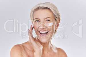 Beauty, skincare and wellness with a senior woman applying lotion, sunscreen or serum to her face in studio on a grey background. Health, skin care and motivation with a beautiful and healthy model